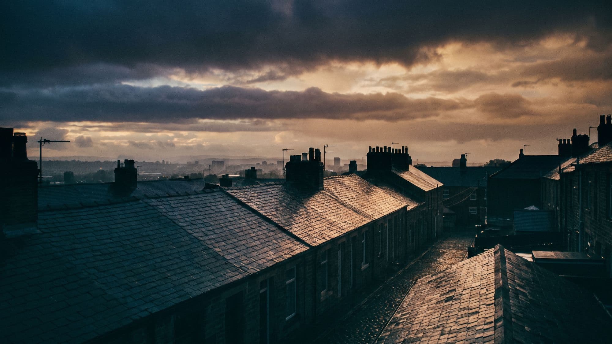 British rooftops beneath a dramatic layered sky just after rain, wet slate catching the light