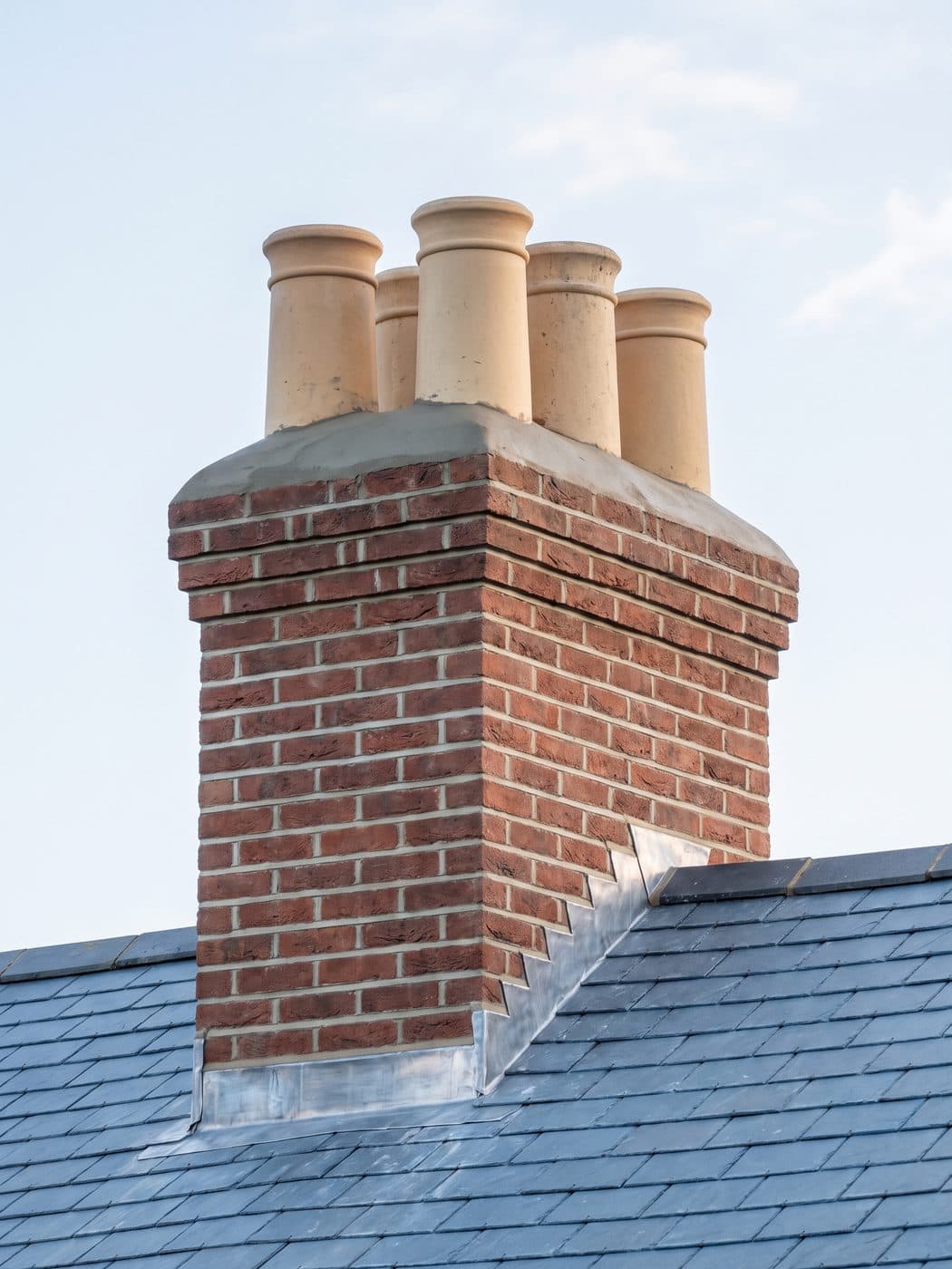 A rebuilt and repointed brick chimney stack with clean clay pots, new flaunching and new lead flashing at its base