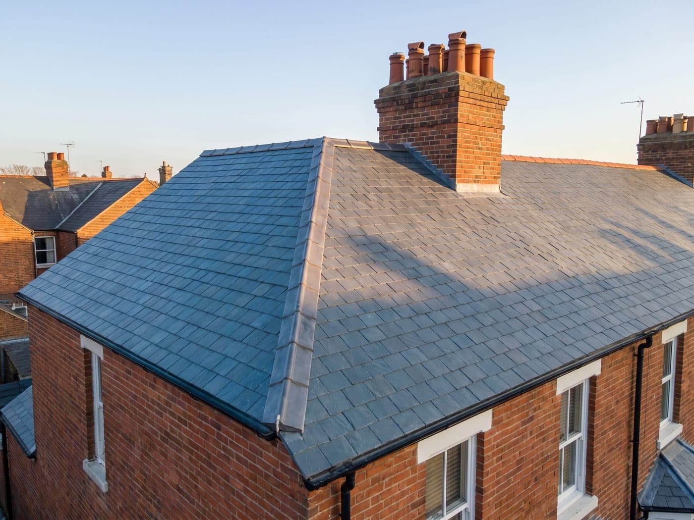 A completed natural slate roof on a Victorian terrace with even courses, a lead ridge and a brick chimney