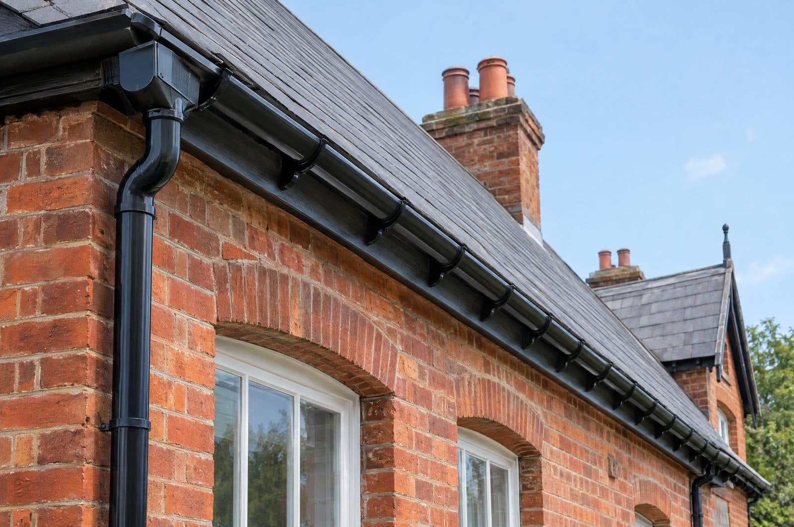 New black half-round guttering and a downpipe along the eaves of a red-brick Victorian house with a slate roof