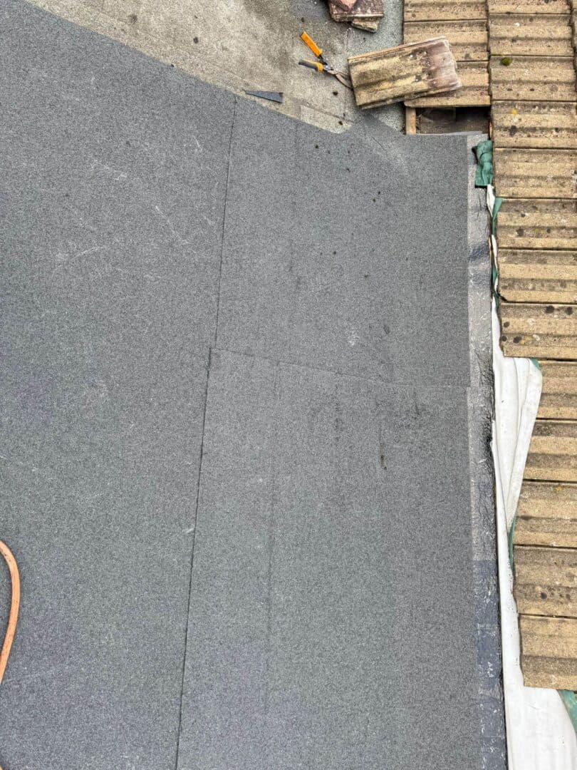 A grey mineral-felt flat roof running up to the edge of a pitched tiled roof