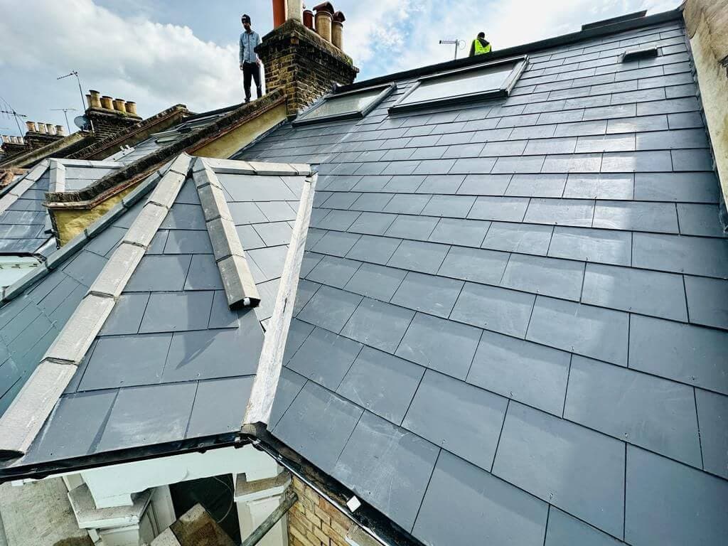 A slate roof with hips and three rooflights, with roofers working on the roof in the background
