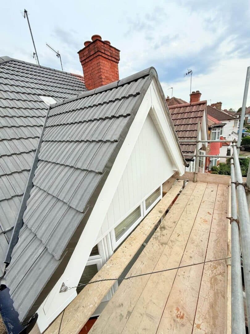 Grey concrete tiles around a gable dormer with white cladding, seen from the scaffold